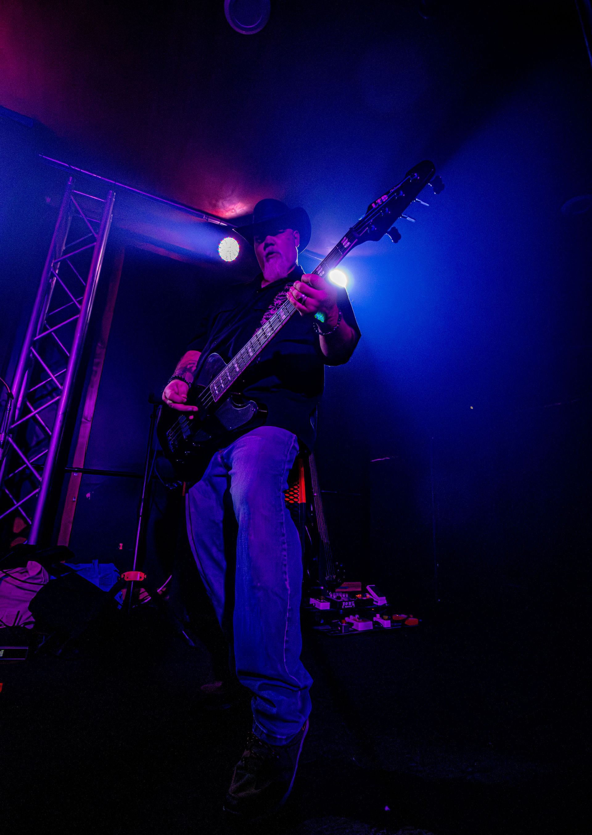 Man playing guitar on stage under blue and purple lights.