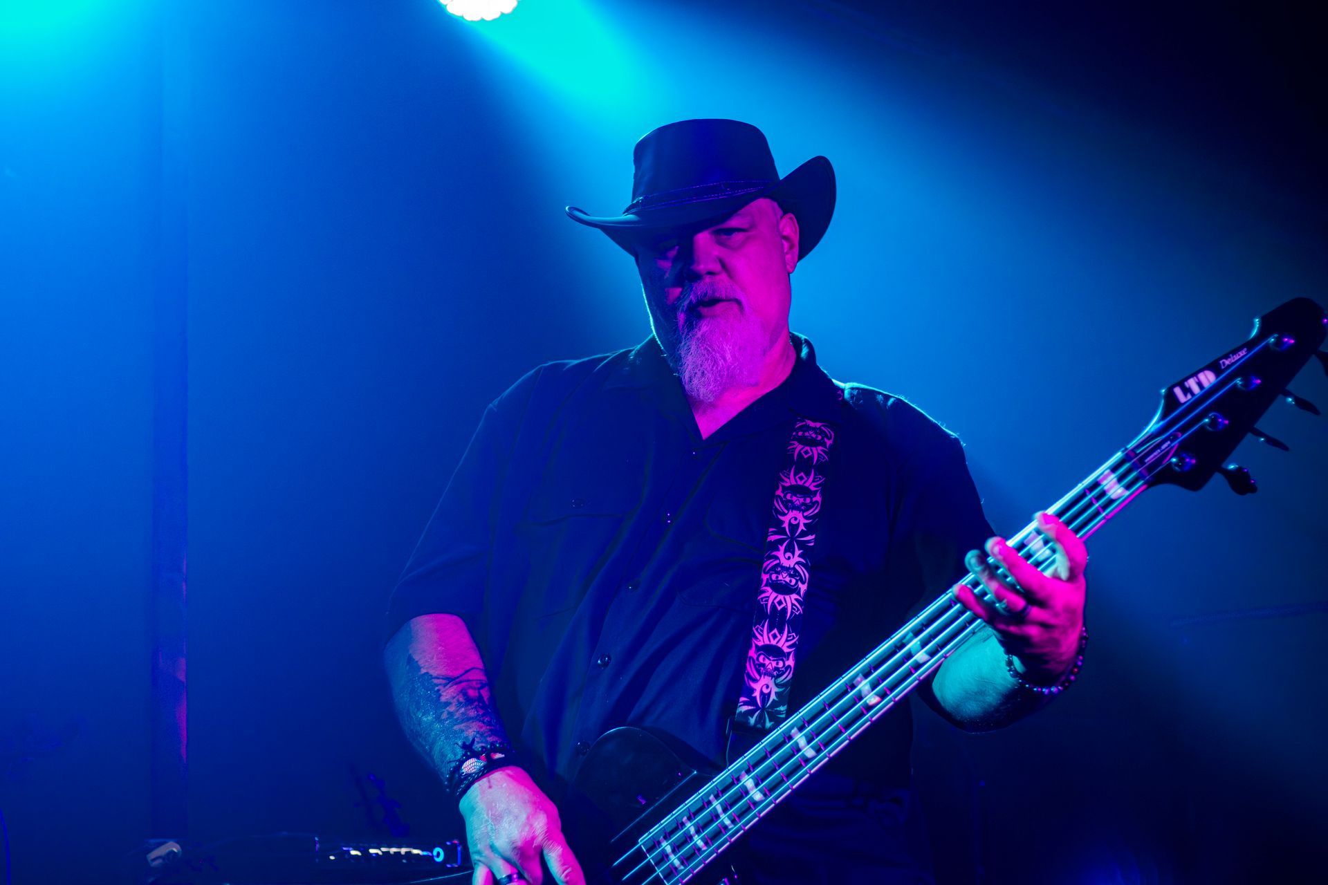 Bass guitarist in a cowboy hat playing on stage under blue and purple lights.