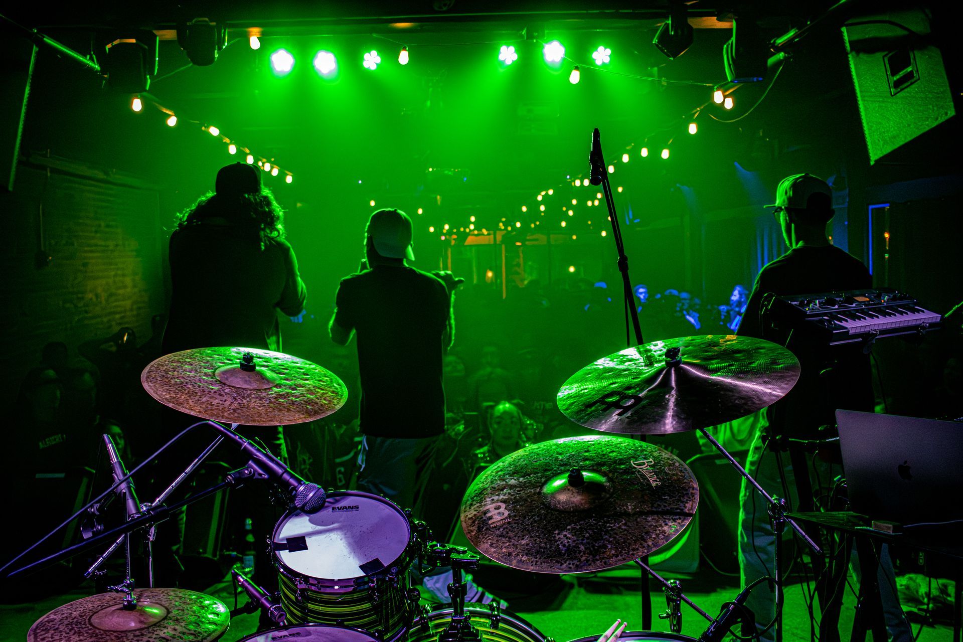 Drum set in front of a band performing on stage under green lights.