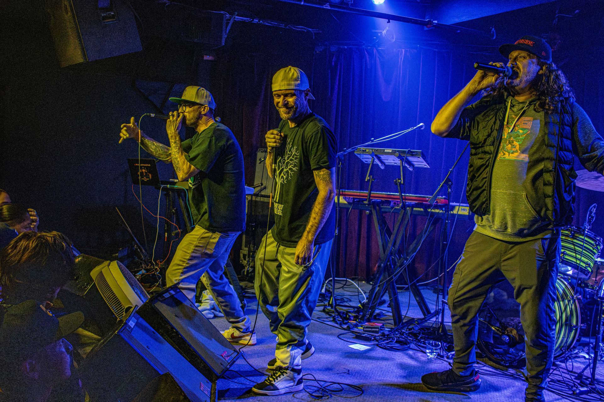 Three people performing on stage with microphones under blue stage lights.
