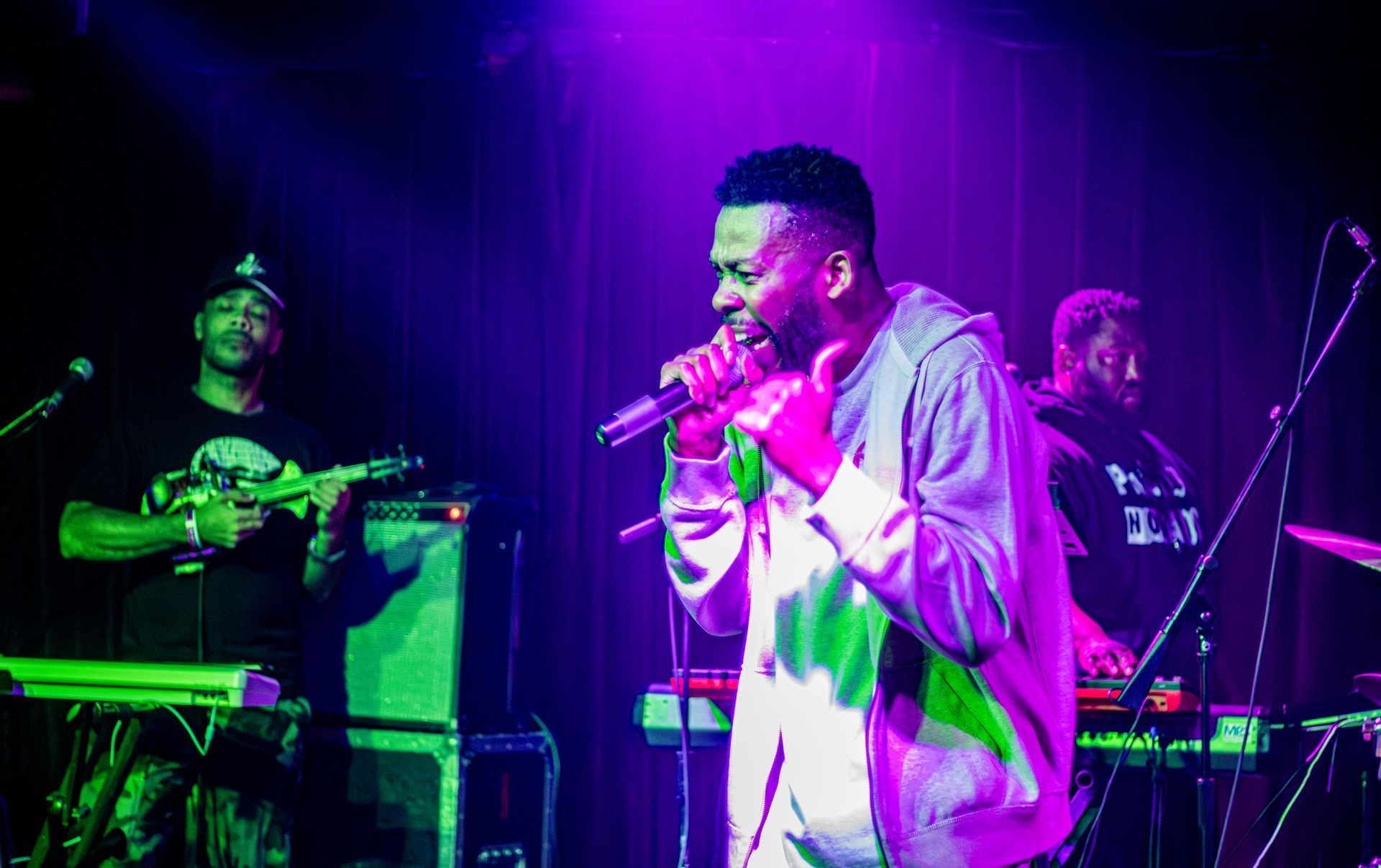 Singer performing on stage with band, lit by purple and green lights.
