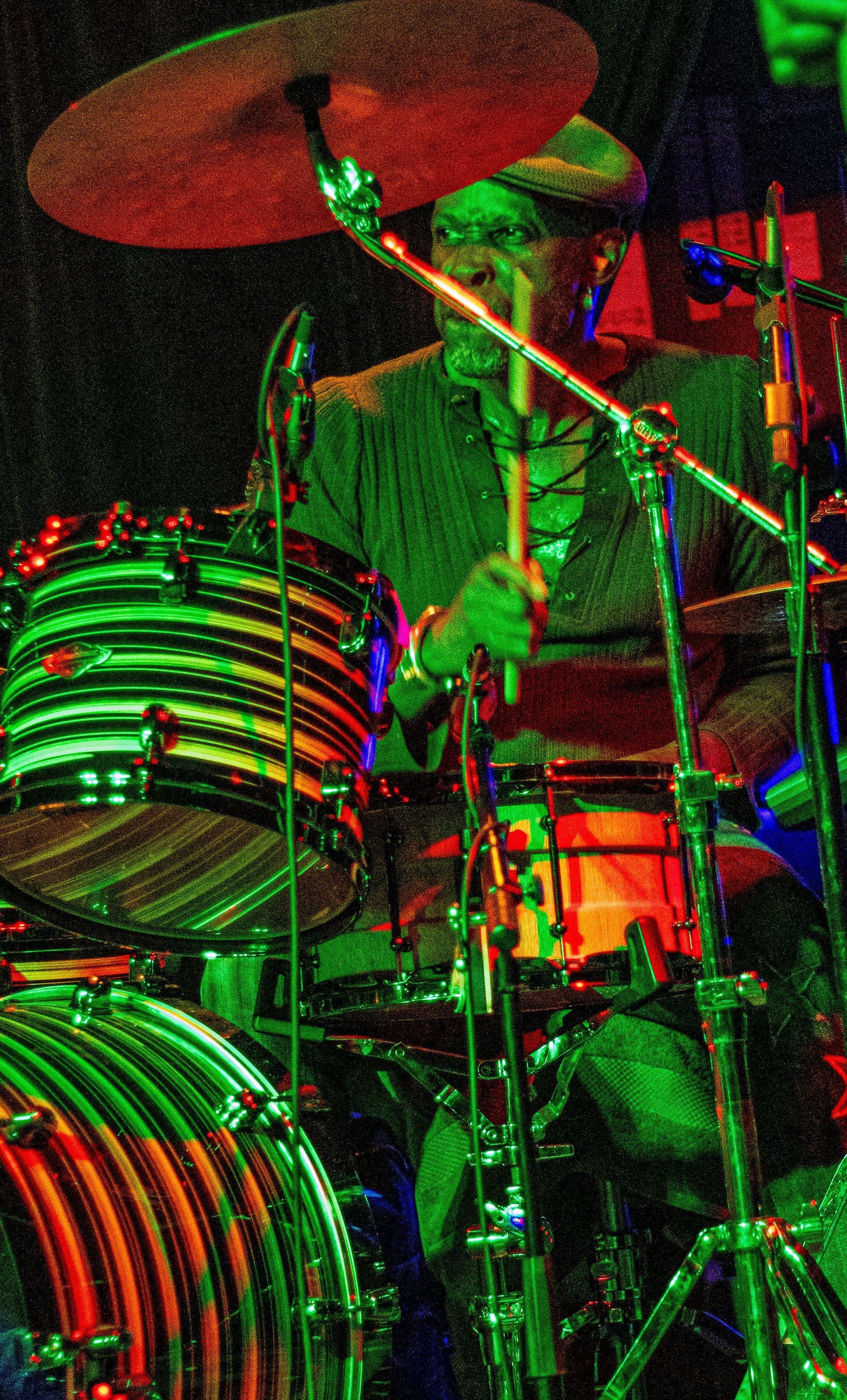 Drummer playing a colorful drum kit, under stage lighting.