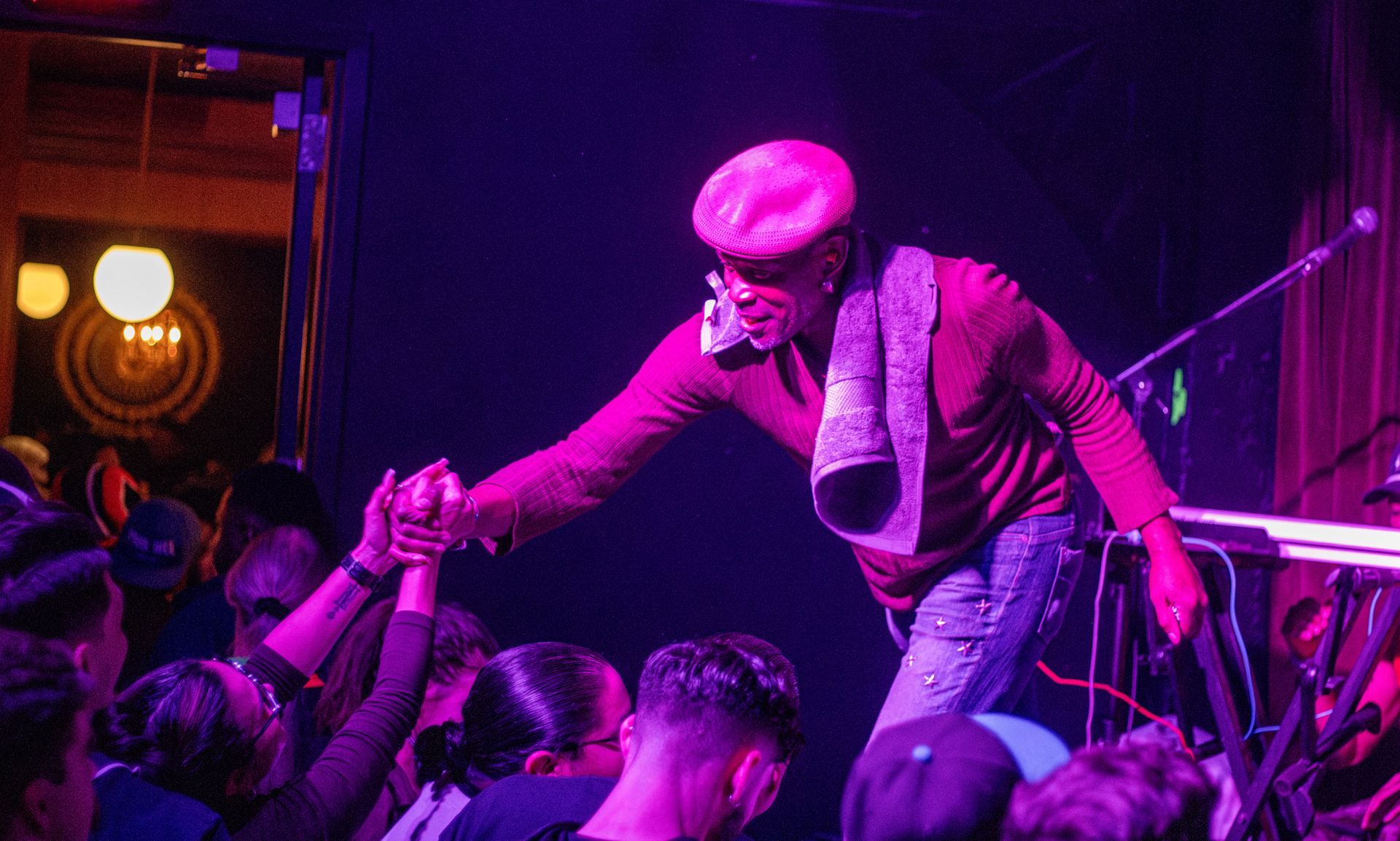 A performer in a pink hat and red outfit reaches out to fans at a dimly lit venue.