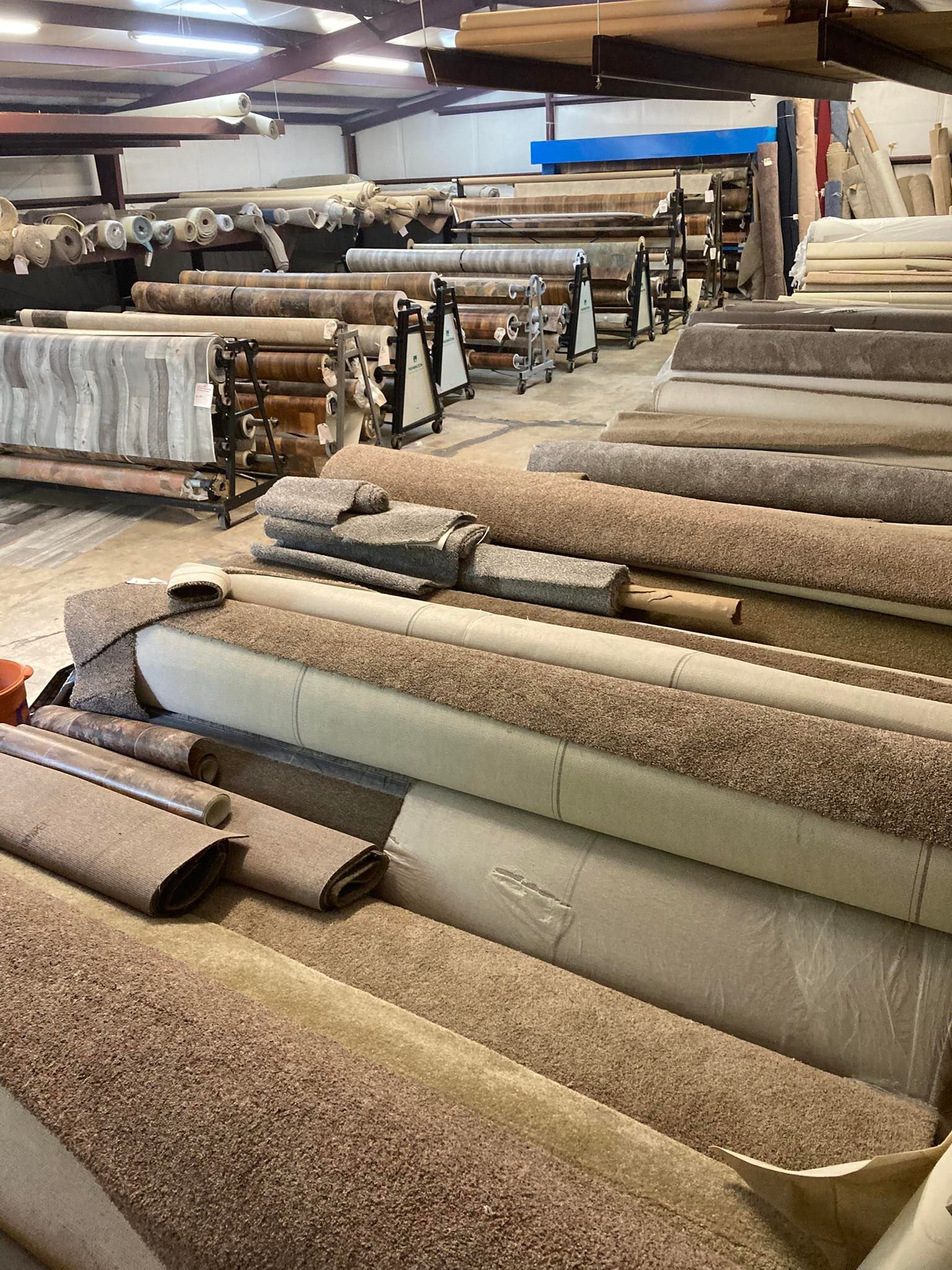 Warehouse interior with numerous rolls of carpet in various colors and textures.