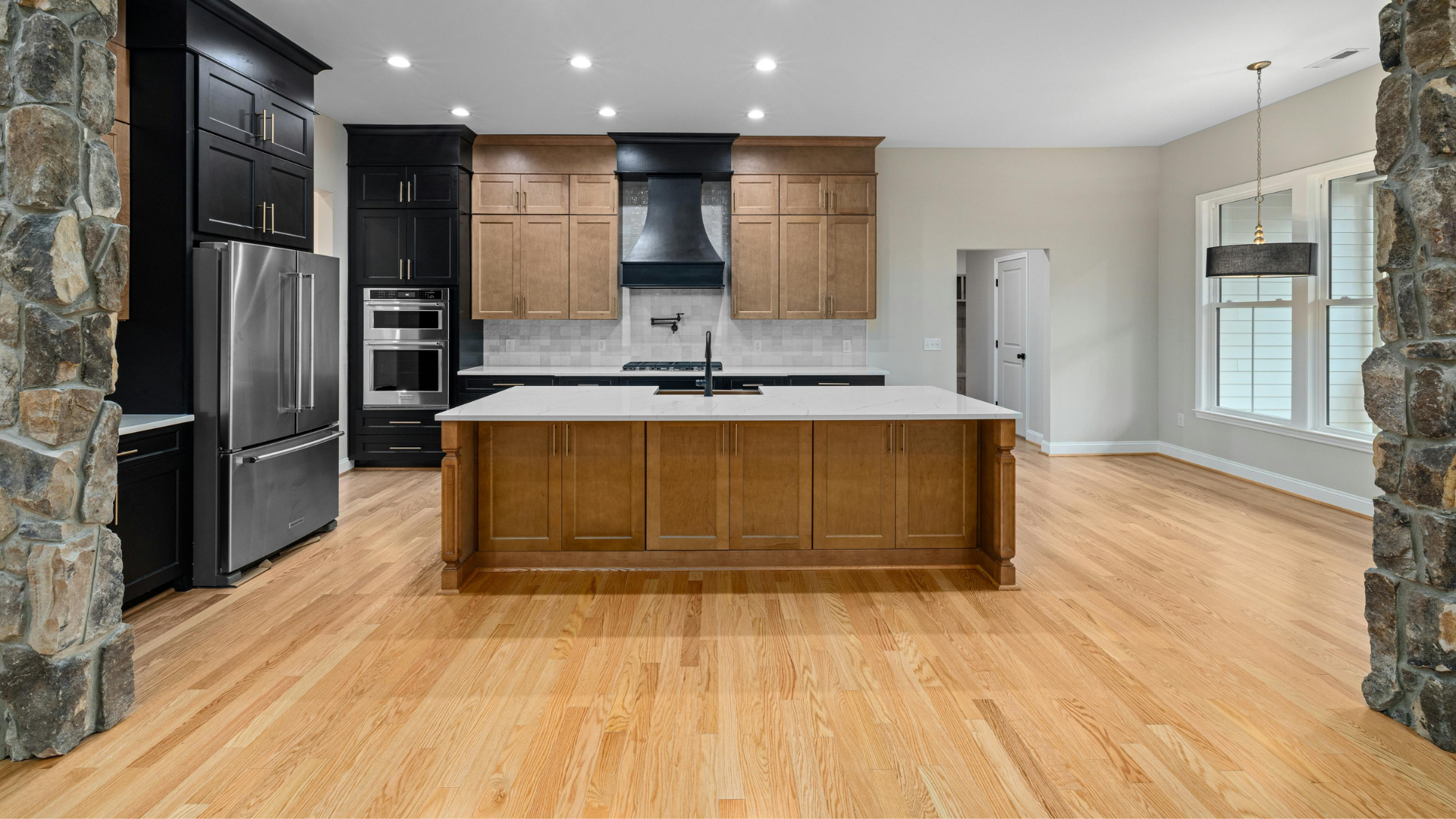 Modern kitchen with light wood cabinets, dark accents, island, stainless steel appliances, and hardwood floors.