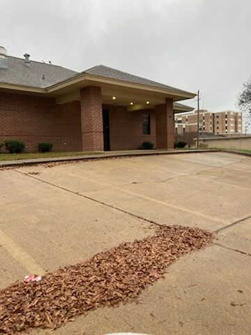 Brick building with covered entrance, empty parking lot, and pile of leaves. Cloudy sky.