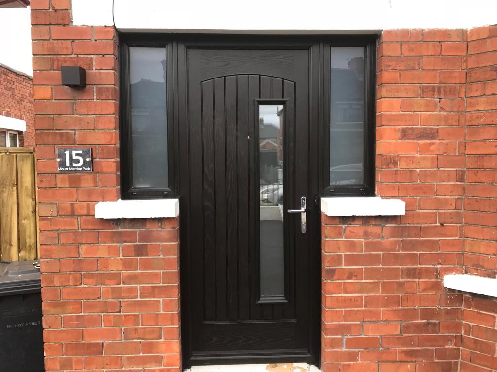 A black door is on a brick wall next to a window.