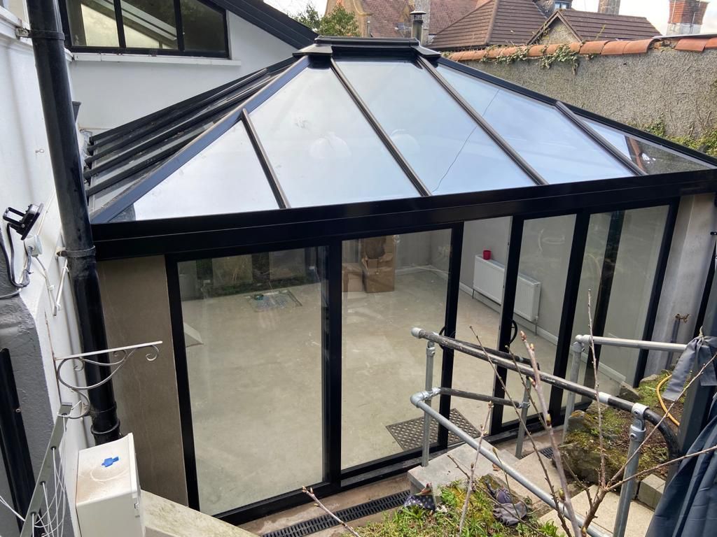 A conservatory with a glass roof and sliding glass doors is being built on the side of a house.