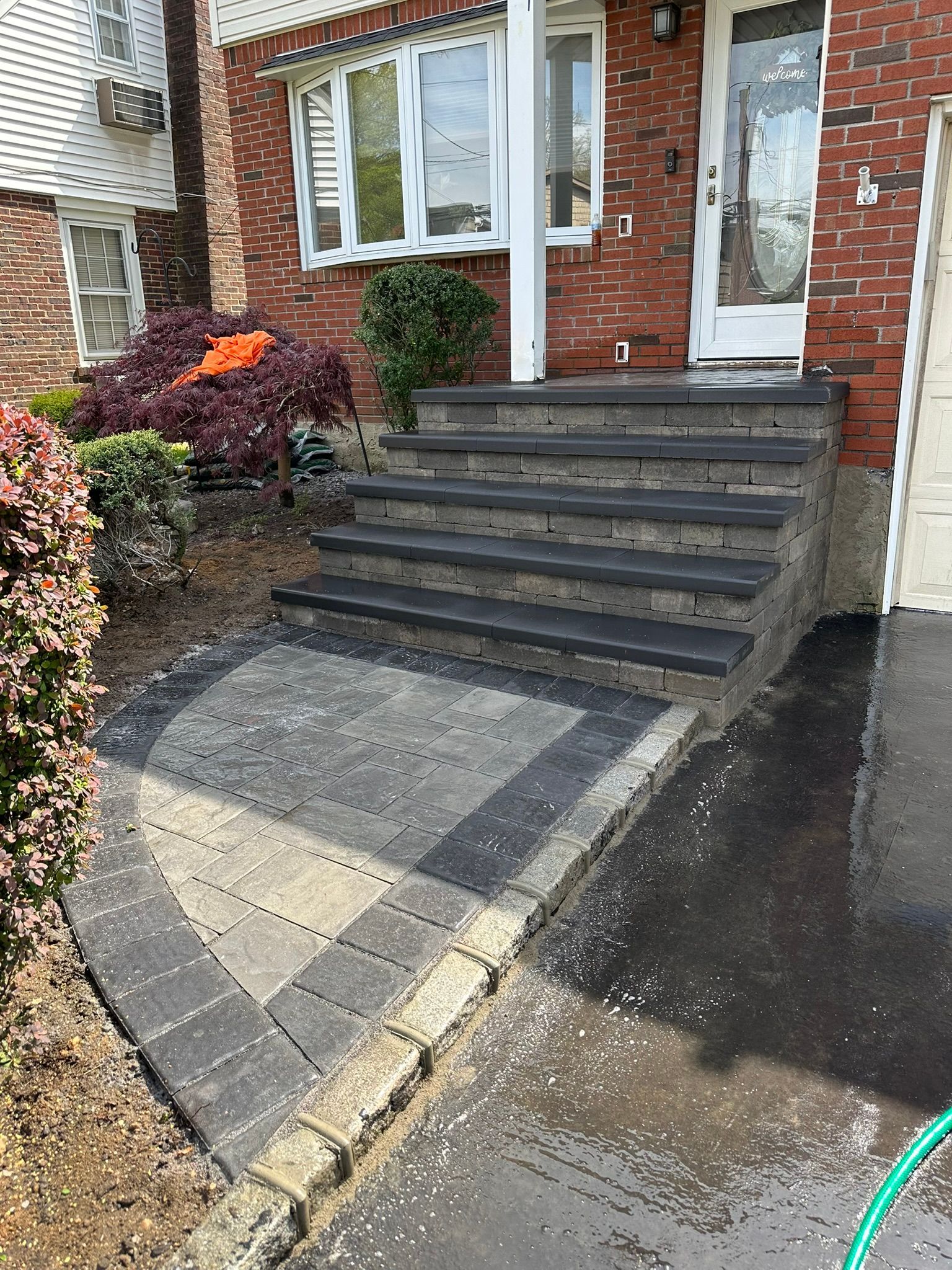 A hose is sitting on the sidewalk in front of a brick house.