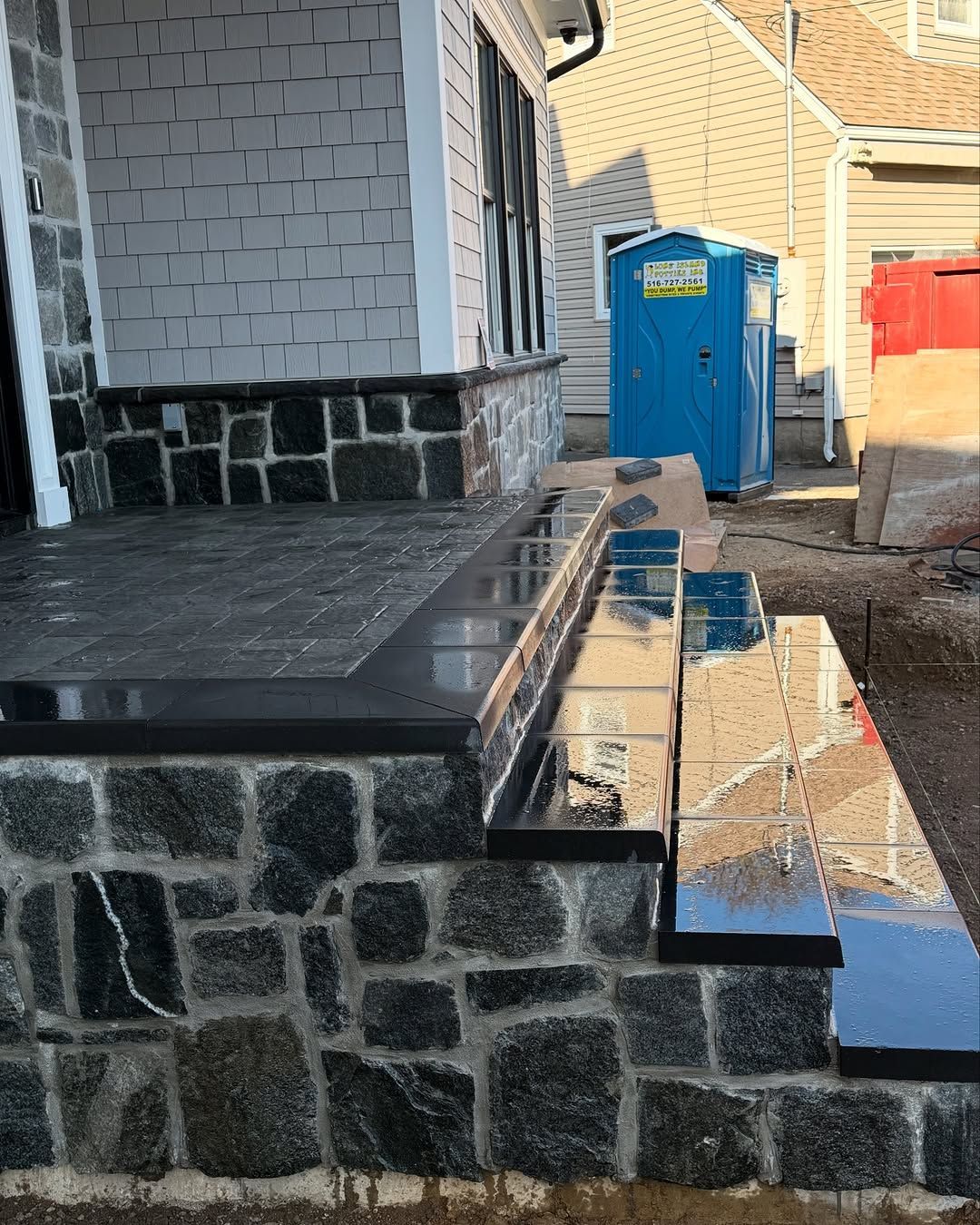 A blue portable toilet is sitting in front of a stone porch.