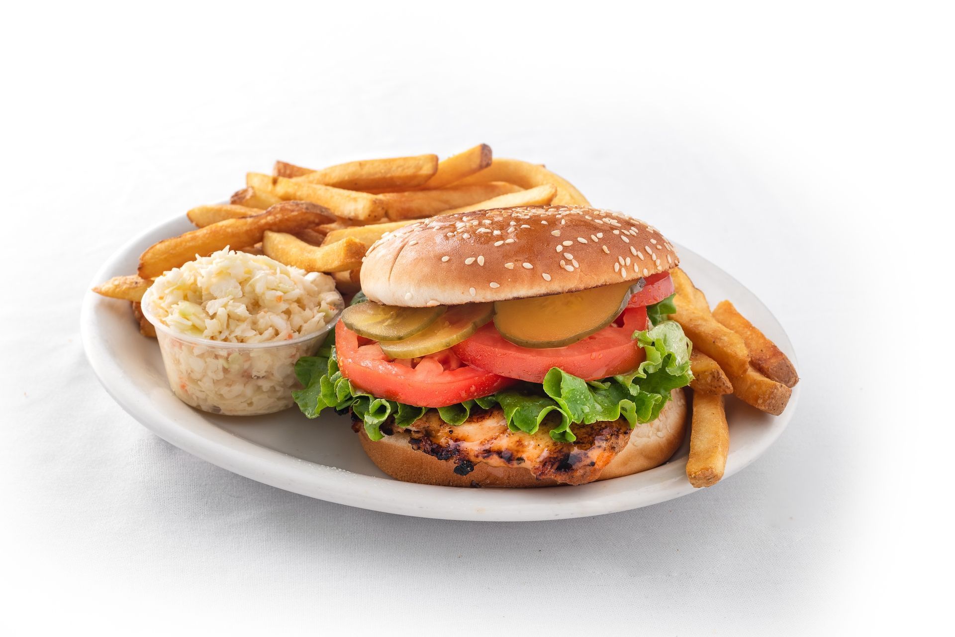 A gilled chicken sandwich and french fries on a white plate.