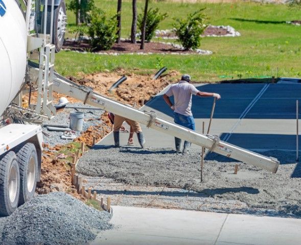 Concrete being poured from a truck, workers leveling the wet cement on a driveway.