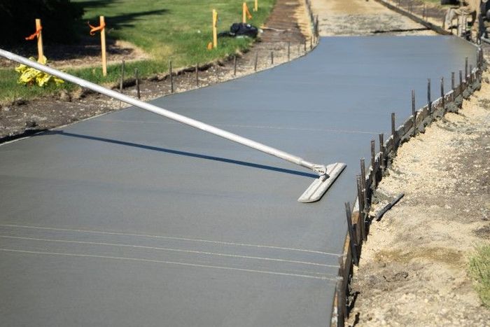 Freshly poured concrete driveway being smoothed with a long-handled screed.