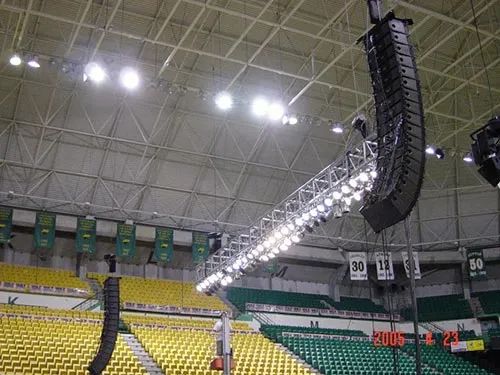 A large speaker is hanging from the ceiling of a stadium.
