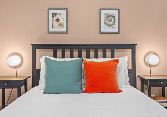 Bedroom with bed, nightstands, lamps, artwork, teal and orange pillows, peach wall.