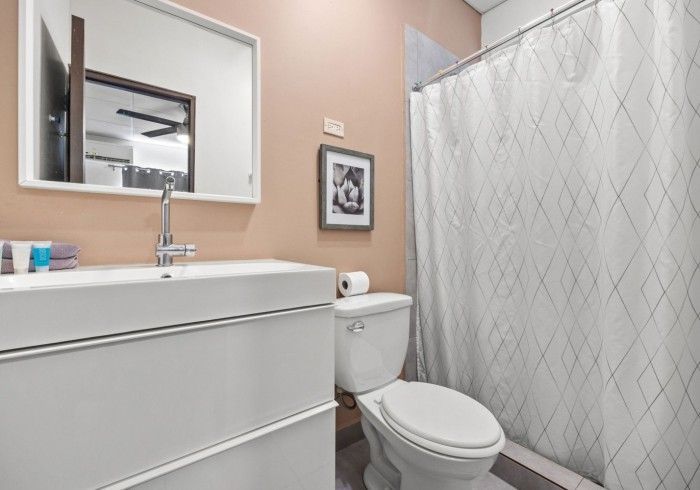 Bathroom with white vanity, toilet, shower curtain, and pink wall.