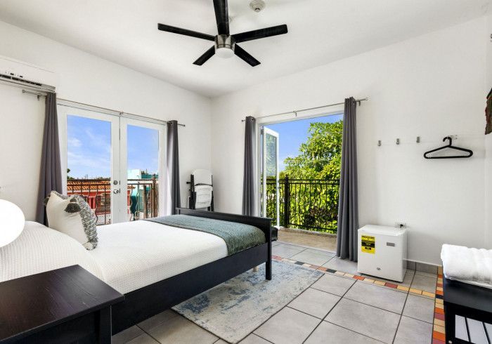 Bedroom with bed, balcony, and open French doors overlooking trees.