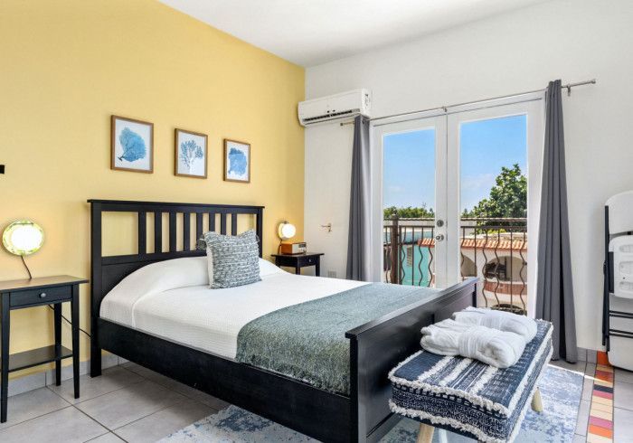 Bedroom with yellow wall, black bed frame, French doors to balcony.