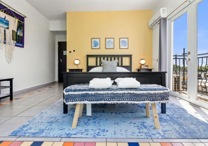 Bedroom with a yellow wall, black bed, blue rug, and balcony access.
