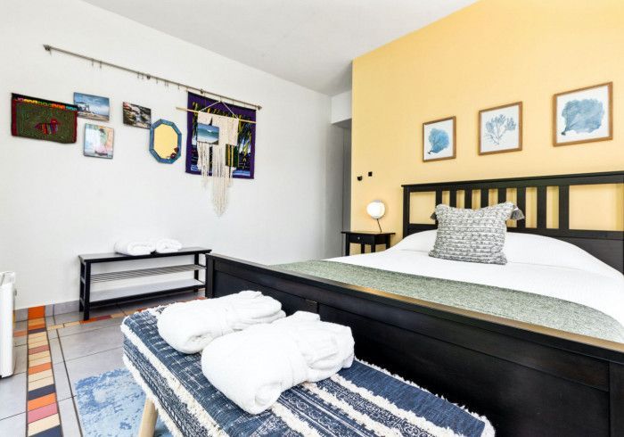 Bedroom with a black bed, bench, and art on the white and yellow walls.