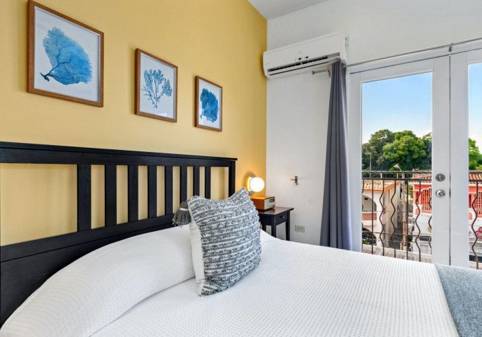 Bedroom with a black bed frame, yellow wall, three blue coral art pieces, and a balcony view.