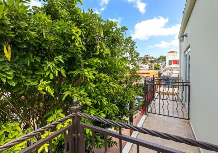 Balcony with wrought iron railing, overlooking a city with a blue sky and trees.