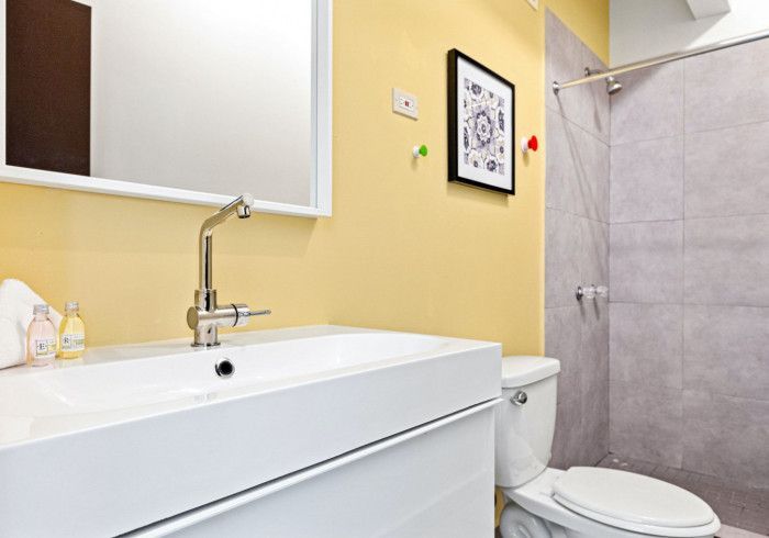 Bathroom with a white sink, toilet, yellow walls, and a grey tiled shower.