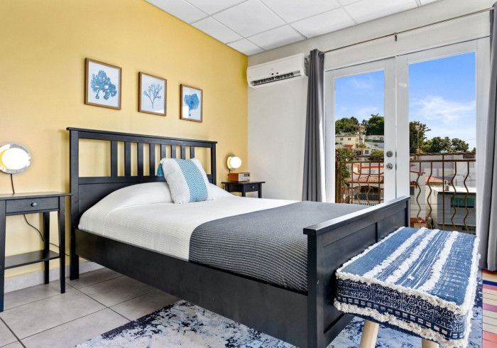 Bedroom with a black bed, yellow walls, and a balcony overlooking a cityscape.