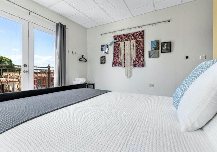 Bedroom with a large bed, balcony, and wall decor. Bright, white walls and bed linens.