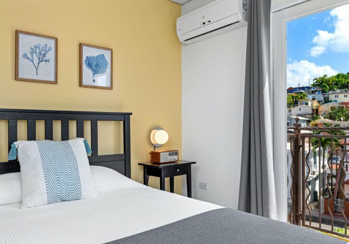 Bedroom with a bed, nightstand, and balcony overlooking a colorful cityscape.
