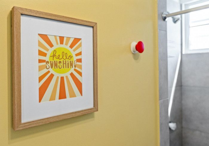 Framed art with a sunburst design on a yellow wall, next to a shower. 