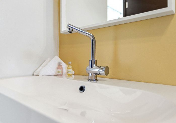 White bathroom sink with chrome faucet, yellow wall, white towel and toiletries.