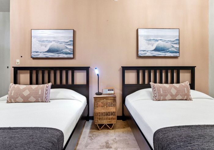Two beds with black headboards, matching artwork, and a shared nightstand in a pink-walled room.