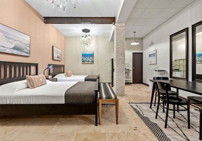 Two beds in a room with a dining area, beige walls, and a chandelier.