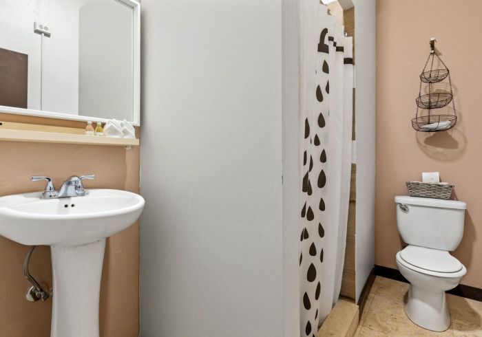 Bathroom with pedestal sink, toilet, and shower curtain with black spots. Peach walls and light floor.