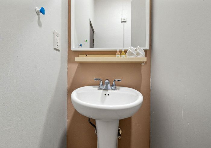 White pedestal sink with mirror and shelf in a small bathroom; tan and gray walls.