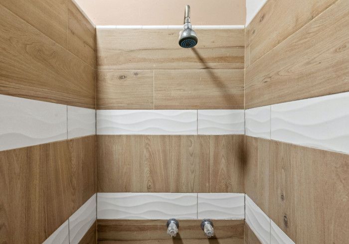 Shower stall with wood-look tiles and wavy white accent tiles, with silver shower fixtures and head.