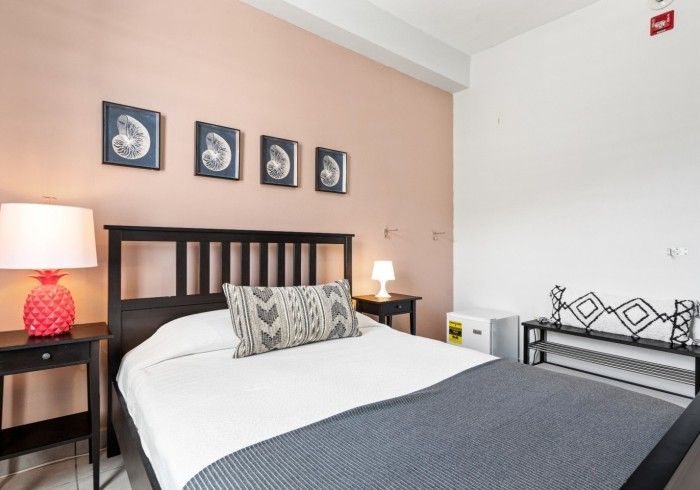 Bedroom with a bed, nightstands, artwork, and a small refrigerator. Pink walls.