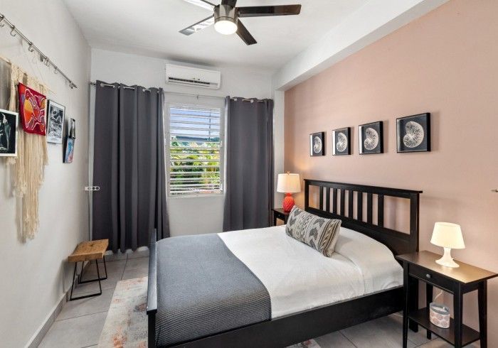 Bedroom with a bed, art, pink wall, gray curtains, and a ceiling fan.