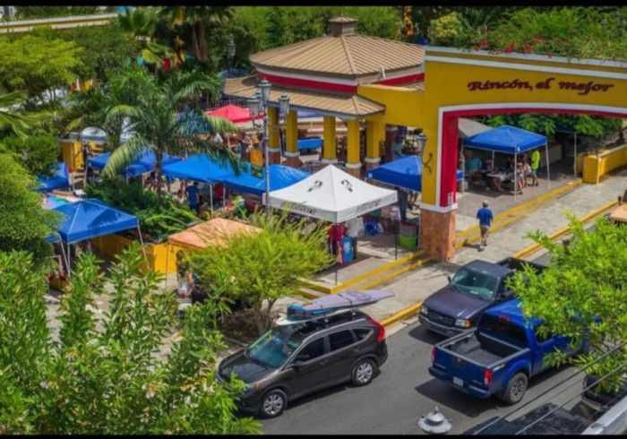 Outdoor market with colorful tents and vehicles parked nearby. 