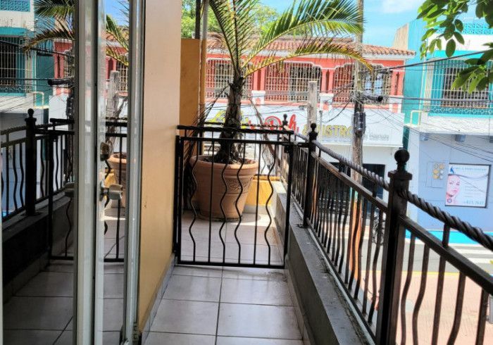 Balcony with wrought iron railing, potted palm tree, and a street view of colorful buildings.