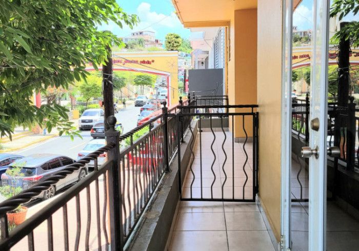 Balcony overlooking a street with cars, trees, and a decorative archway.