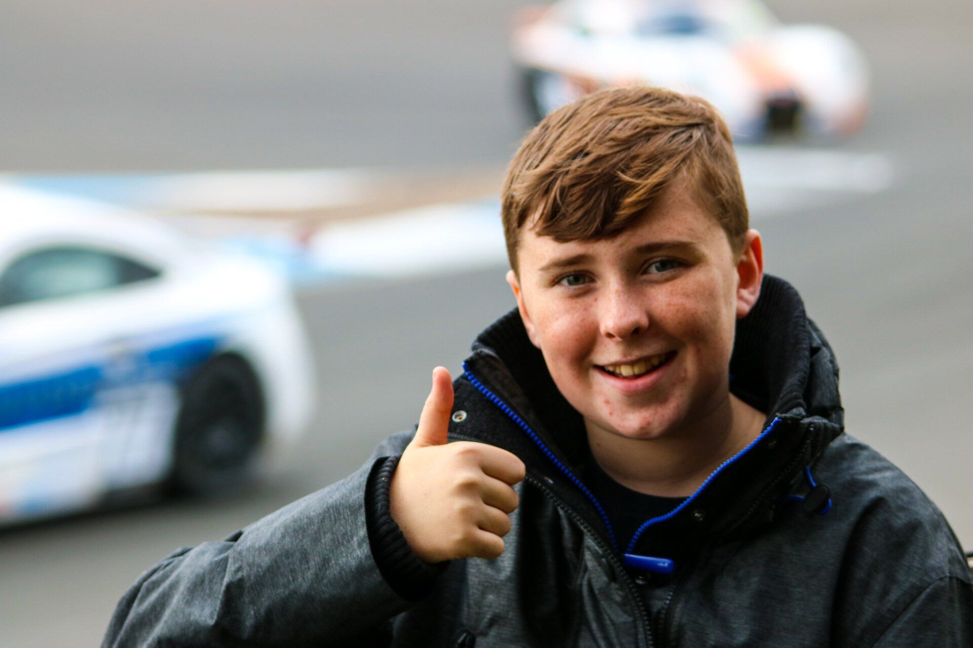 A young boy giving a thumbs up in front of a race car