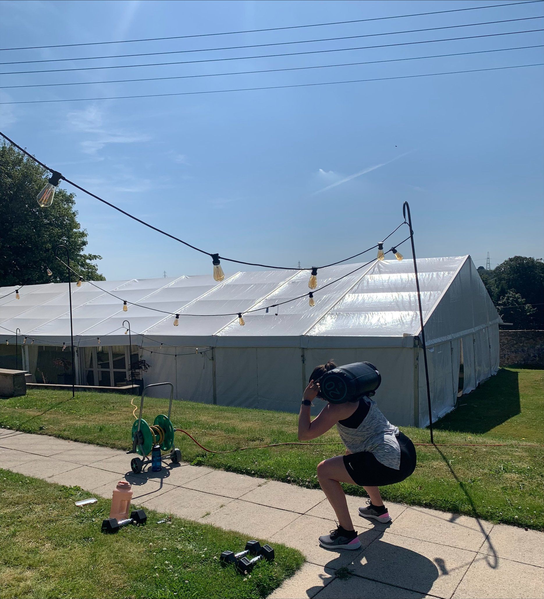 A person squatting with a bag on their back in front of a white tent