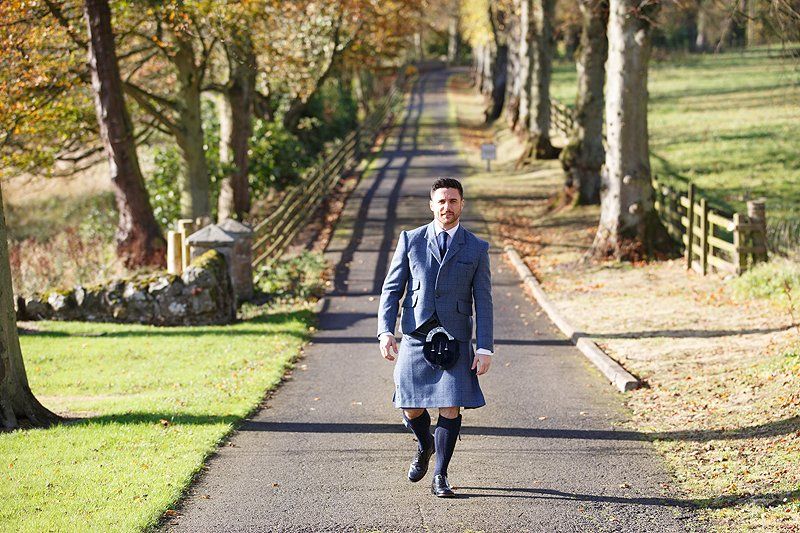 A man in a kilt is walking down a road