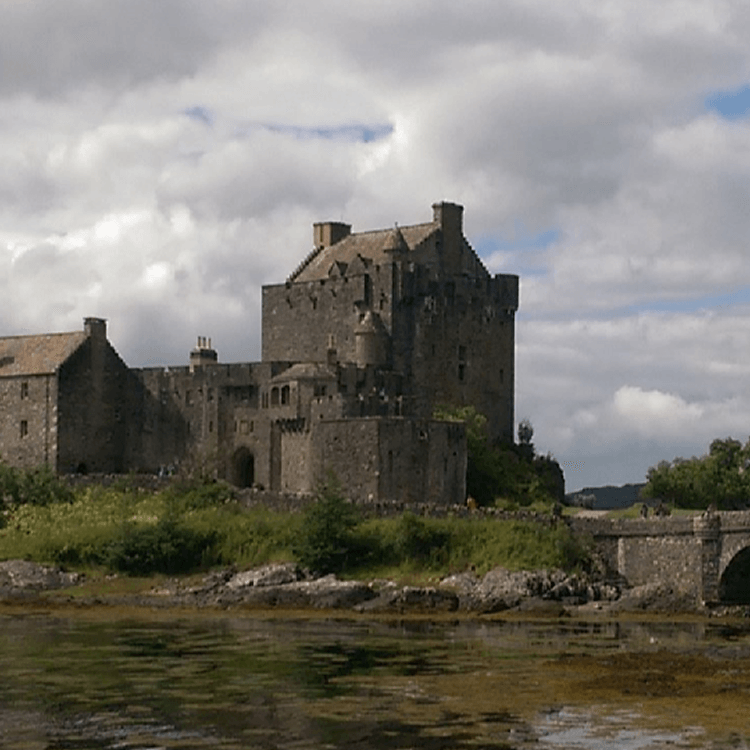 A large castle sits on a hill overlooking a body of water