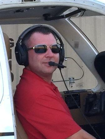 A man wearing headphones and sunglasses is sitting in the cockpit of an airplane.