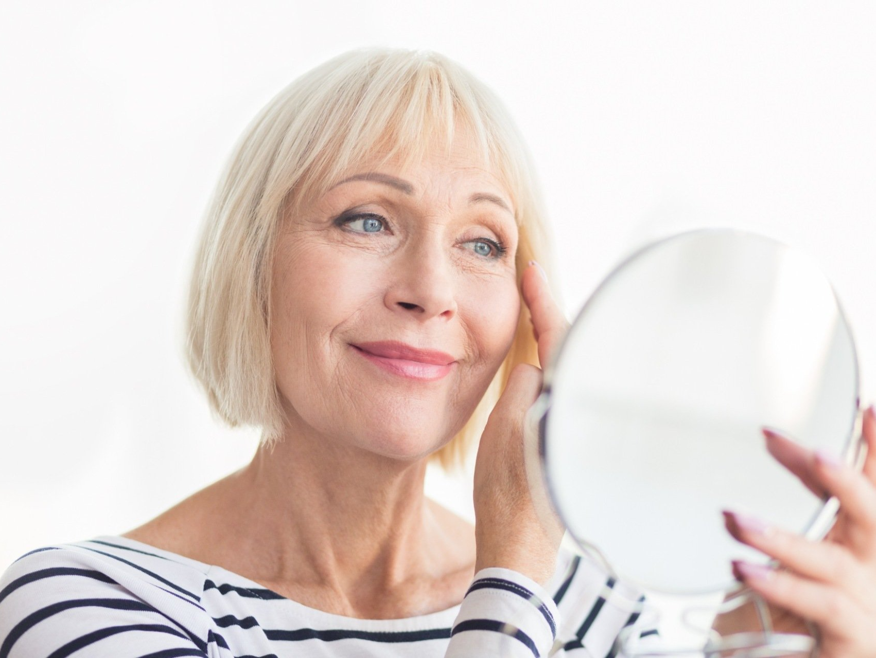 senior woman admiring skin in handheld mirror