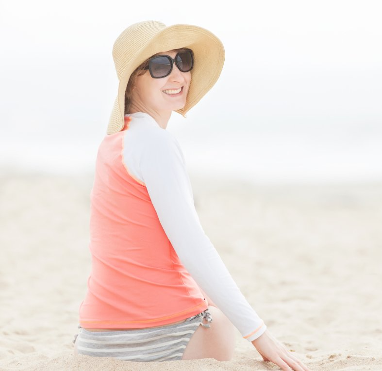 woman sitting on beach with sunhat and rashguard