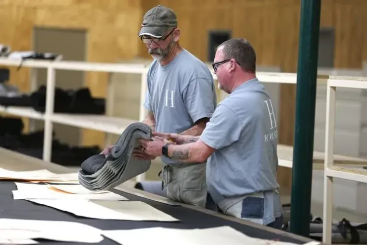Two people in matching gray shirts work together to fold a stack of gray fabric in a warehouse-like setting.